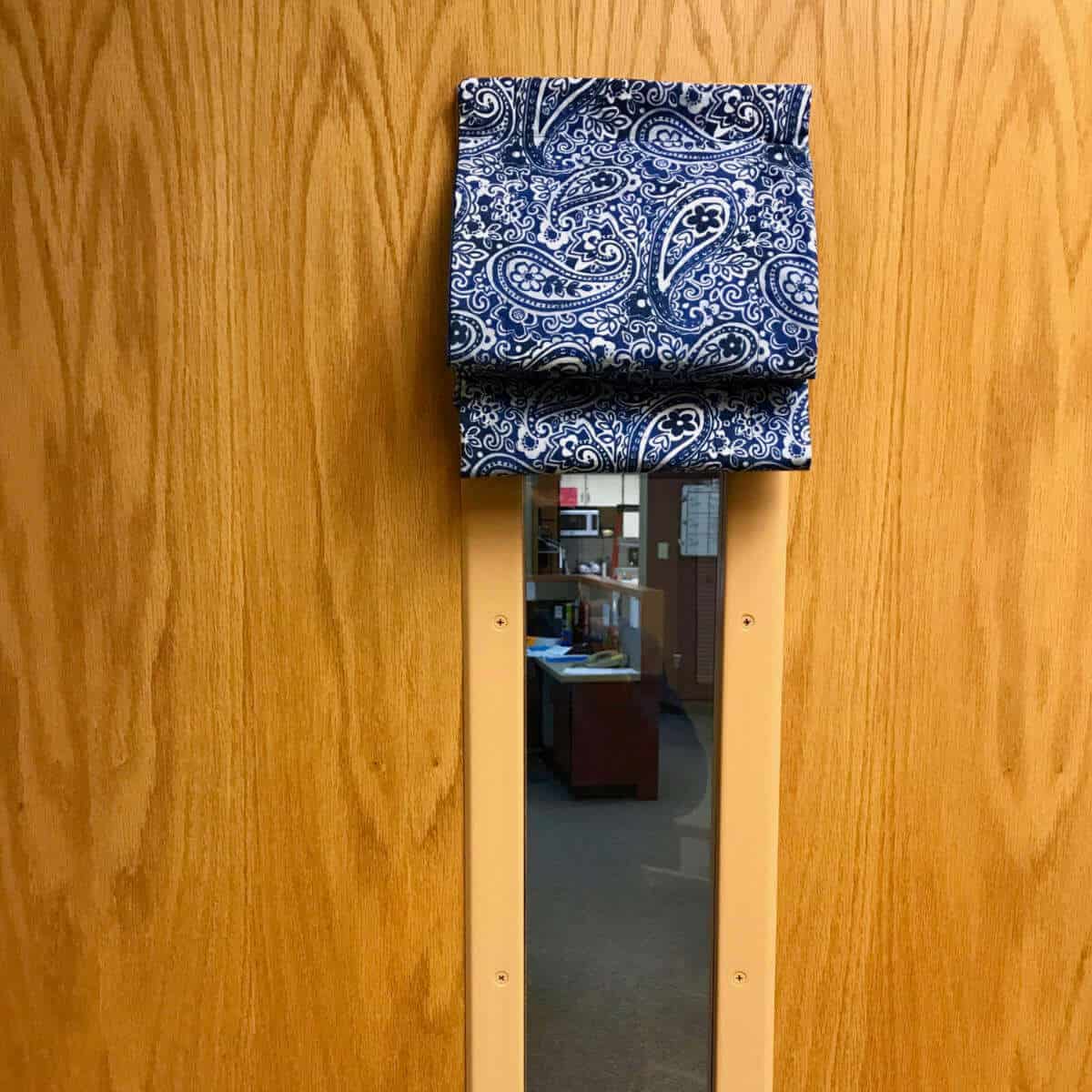 Classroom door with a window and a curtain pushed up on the window.