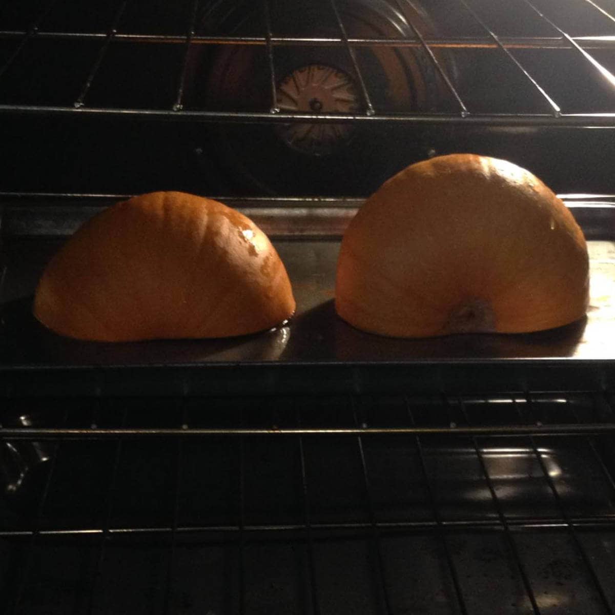 Two halves of a pumpkin sitting face down on a cooking sheet in the oven.