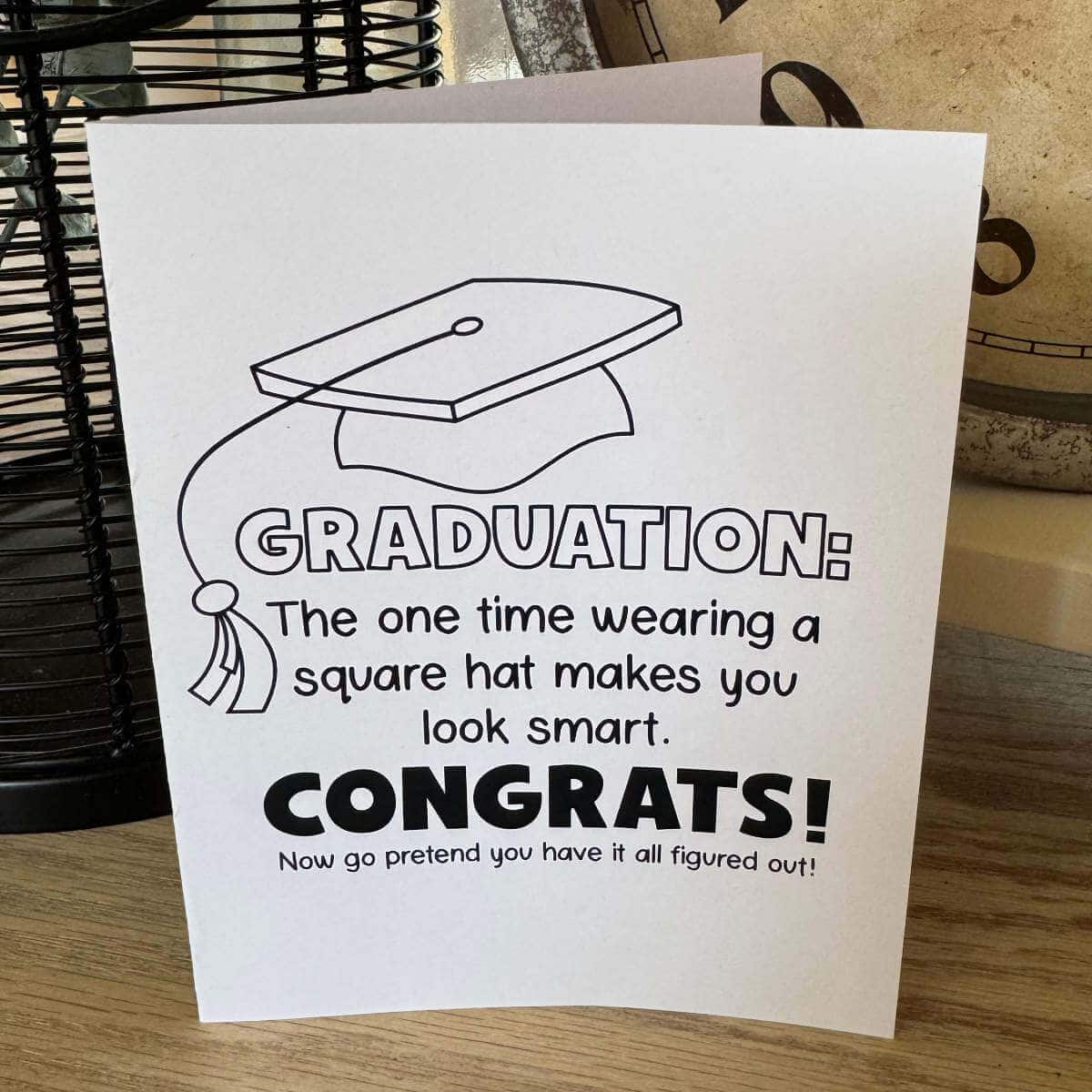Printable graduation card sitting on a table with a clock behind it.