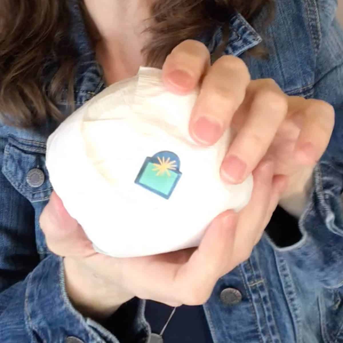 Girl holding a snowball made out of white paper streamer that has a Christmas sticker on it.