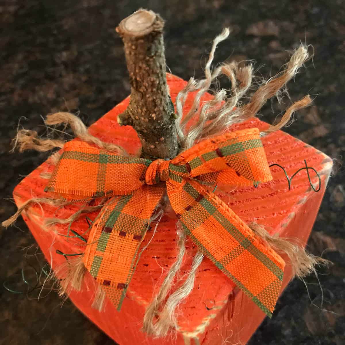 Three 4 x 4 wood pumpkins with stems and bows on a coffee table.