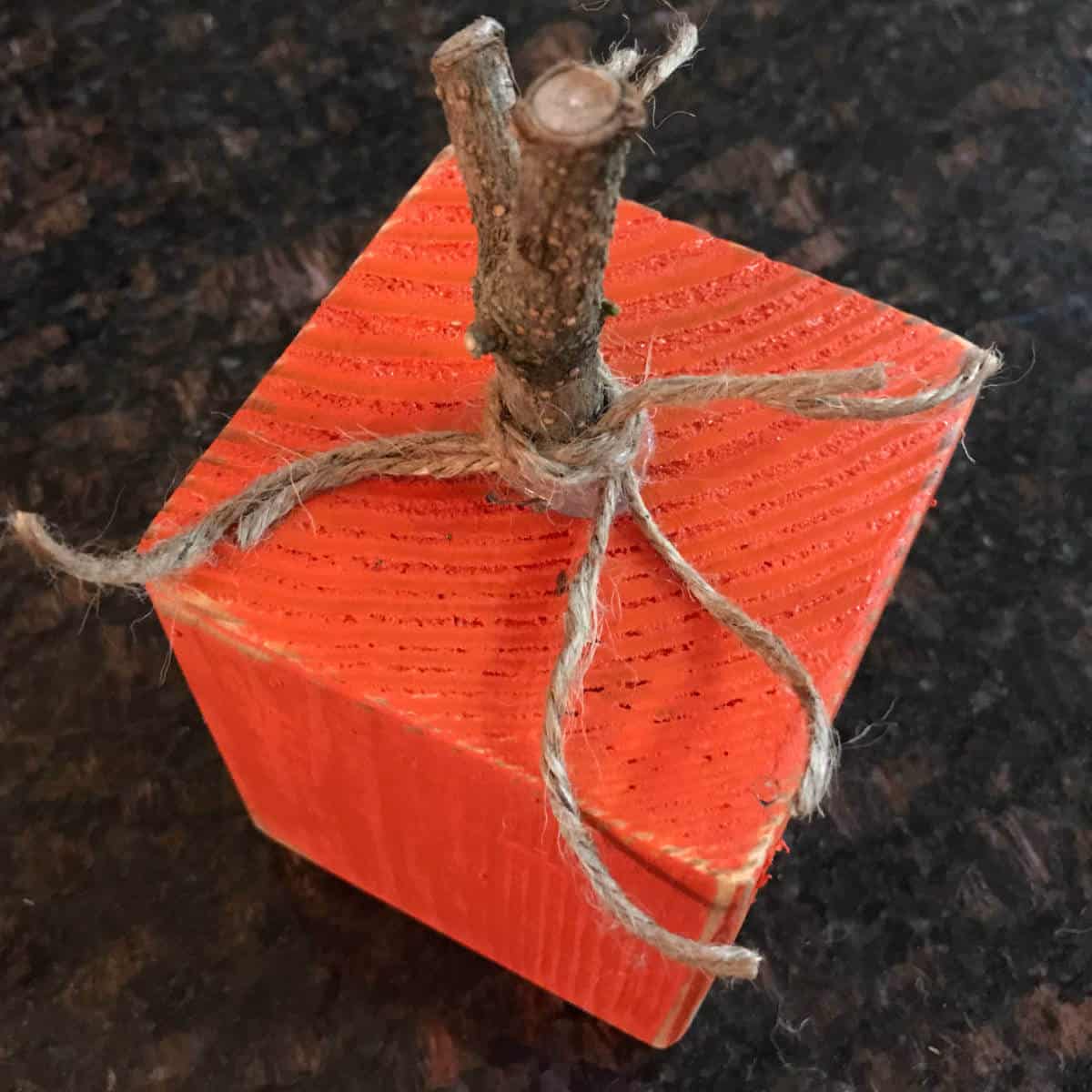 4 x 4 wood block painted orange with a wood stem and jute tied around the stem.