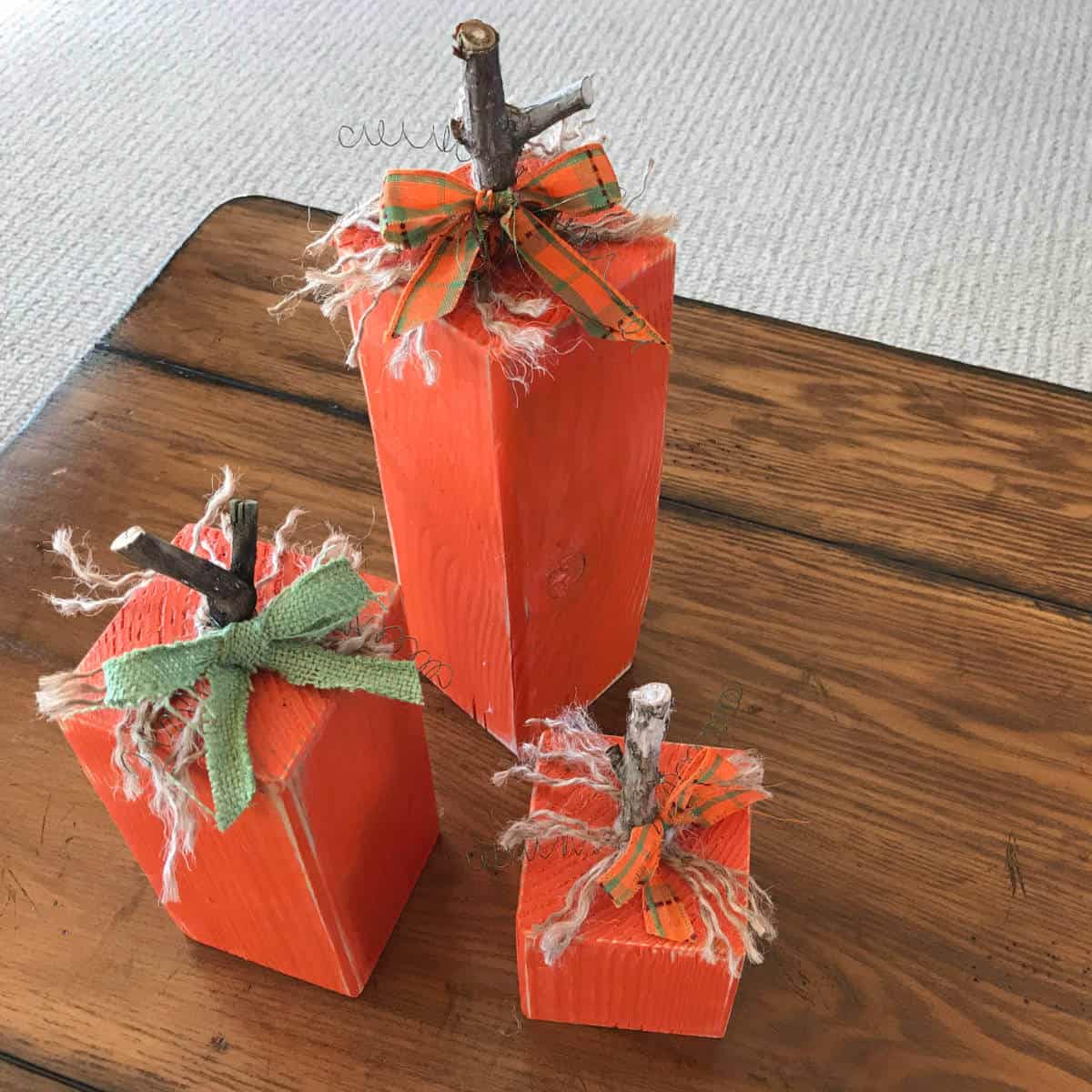 Set of three pumpkins created by painting 4 x 4 blocks orange and adding a stem, jute, and ribbon.