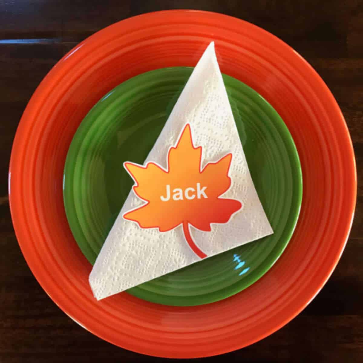 Orange plate with a small green plate on top of it, then a white napkin, and a paper fall leaf with the name, Jack, on it.