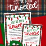 Image of a You've Been Tinseled printable in two sizes on top of a clipart Christmas gift.