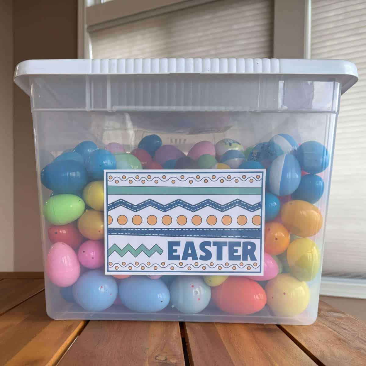 Clear storage bin full of plastic Easter eggs with a printable Easter label on the end.