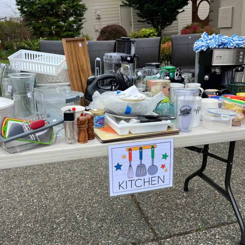 Garage sale table with kitchen goods on it and a sign that says, Kitchen.