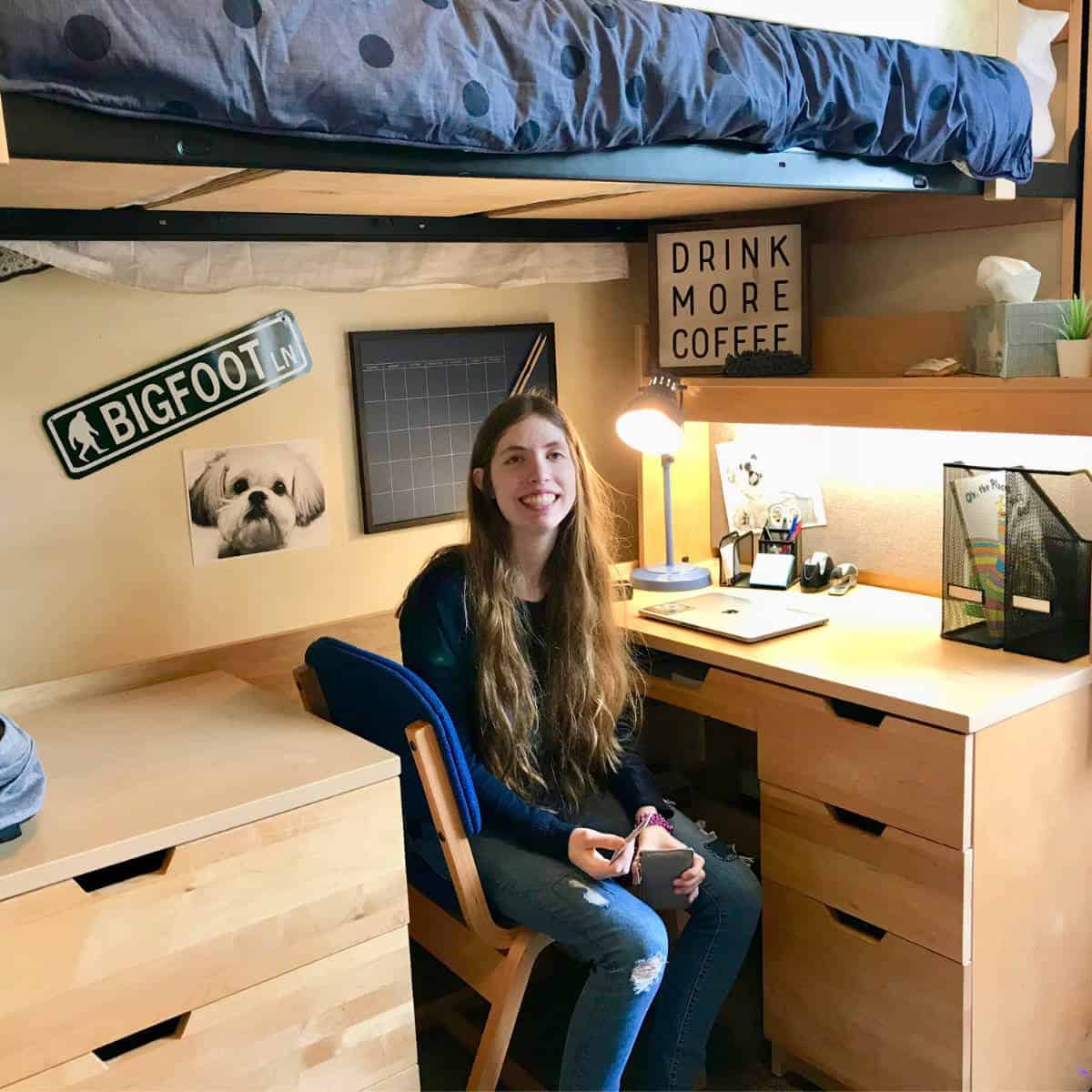 Image of a girl sitting at a desk under her bed in a college dorm room.