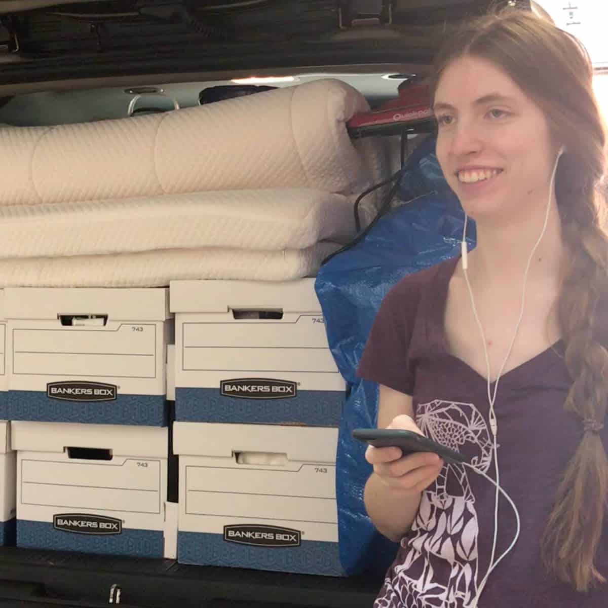 Image of a college student standing at the back of her mom's SUV full of boxes and a mattress topper.