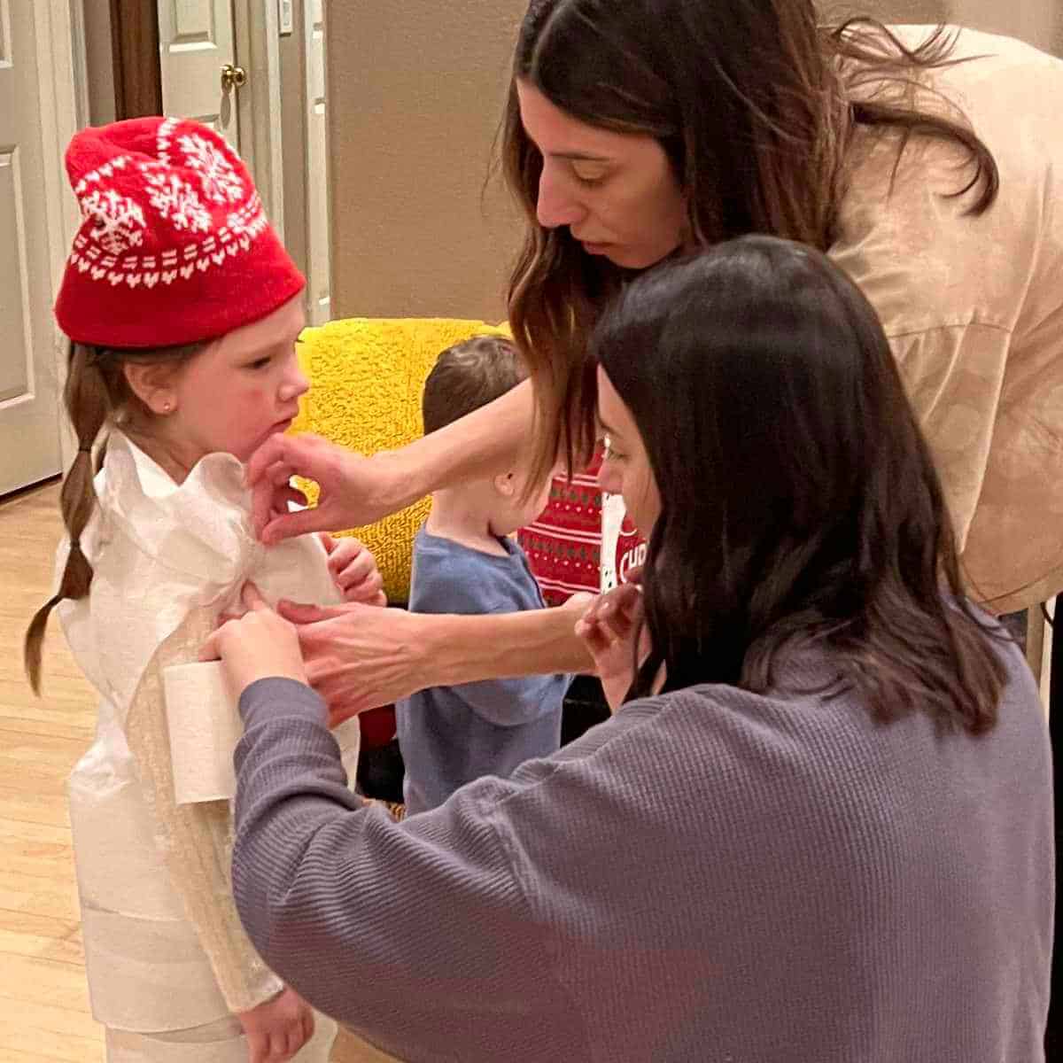 Dressing a girl as a snowman using toilet paper and provided supplies.