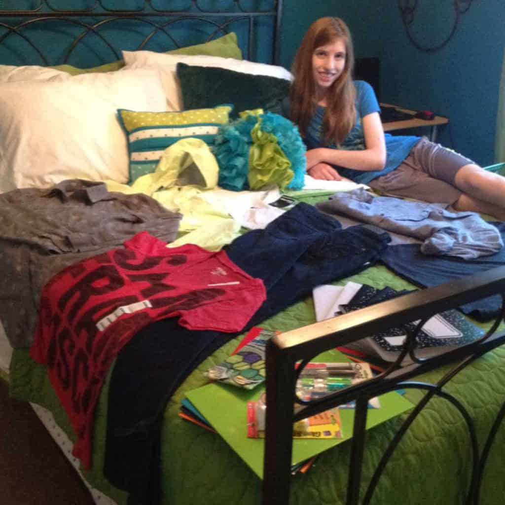 Girl sitting on her bed with her new school clothes arranged on the bed.