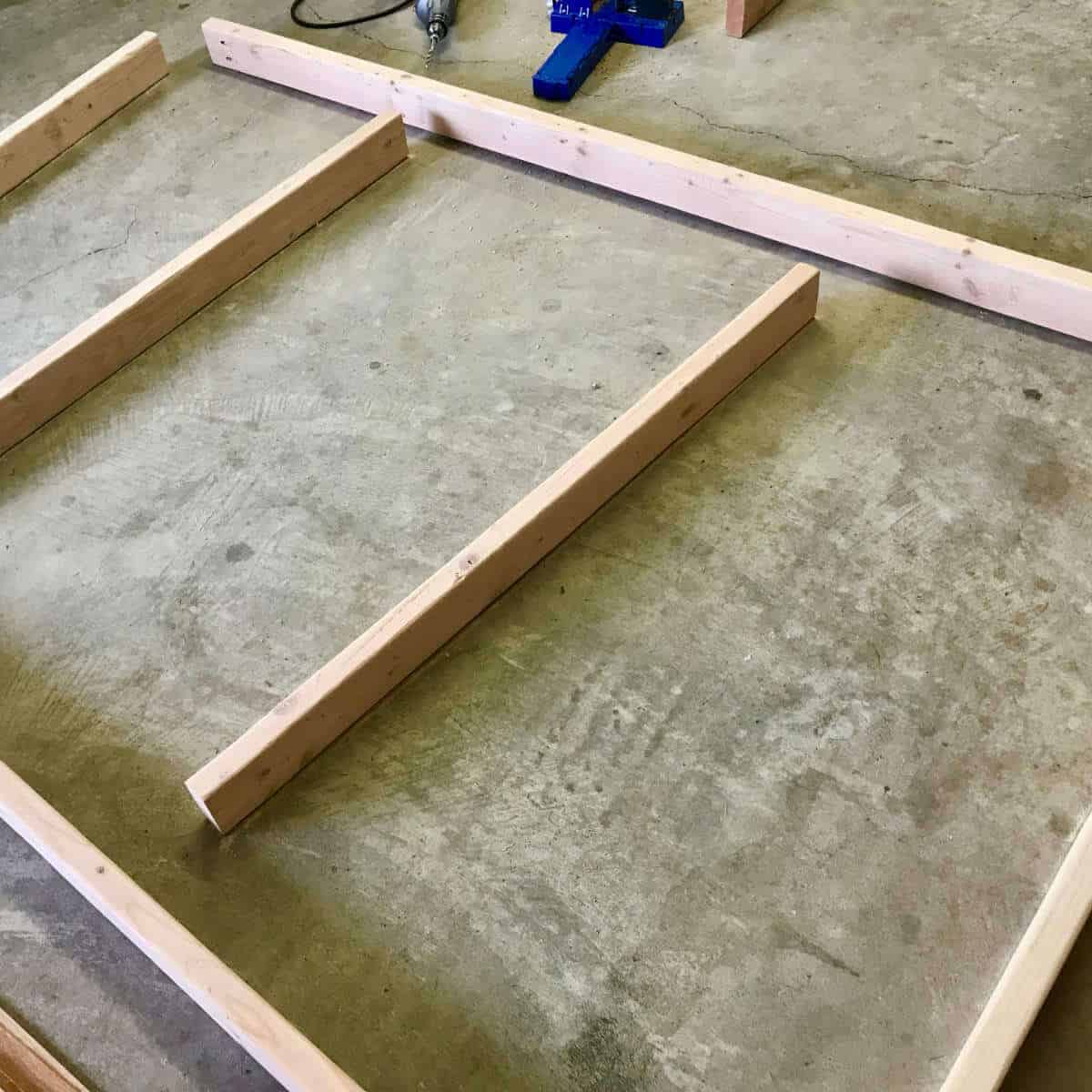 Framing boards laid out on a concrete garage floor for a backdrop wall.