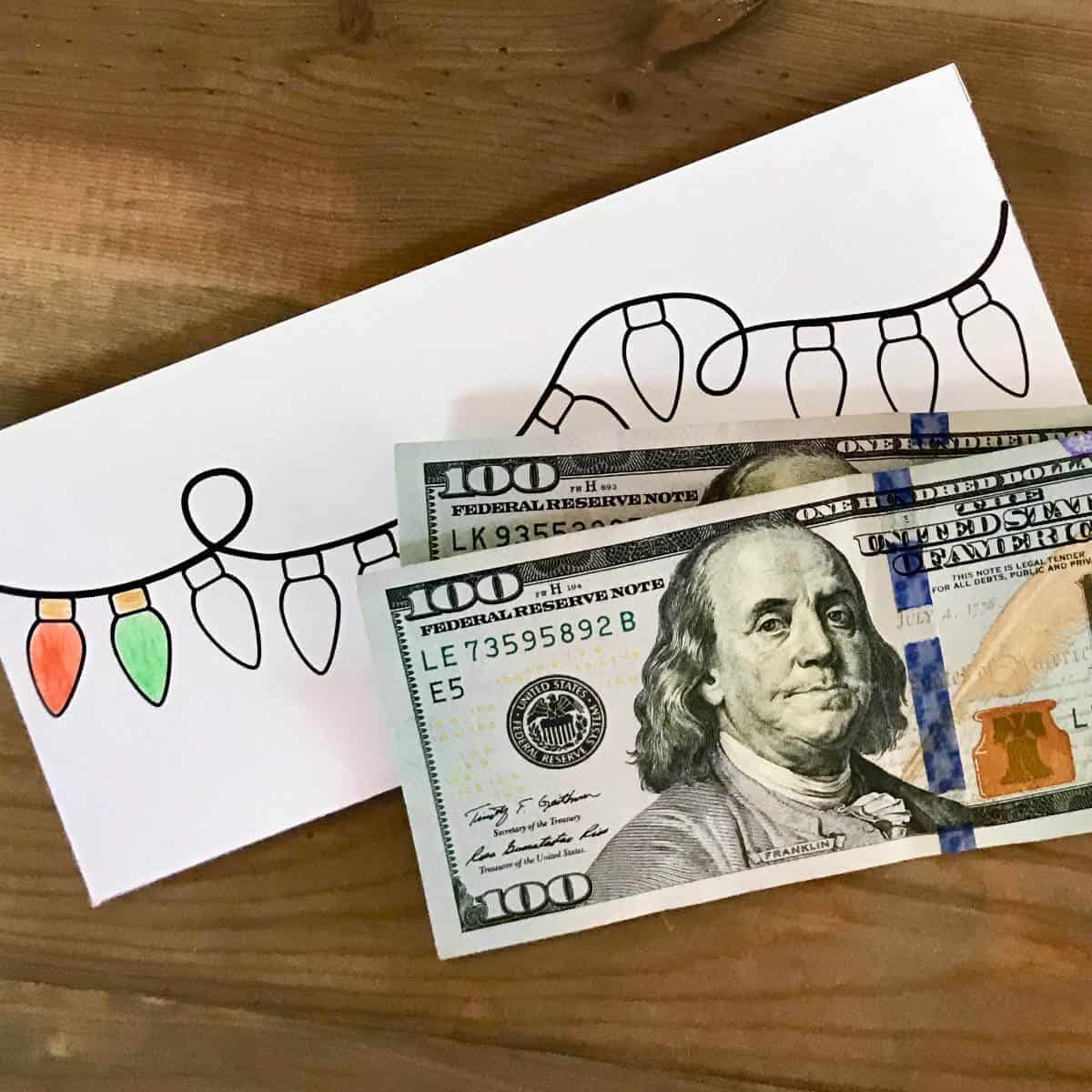 Image of two $100 dollar bills in front of a printable Christmas savings tracker envelope.