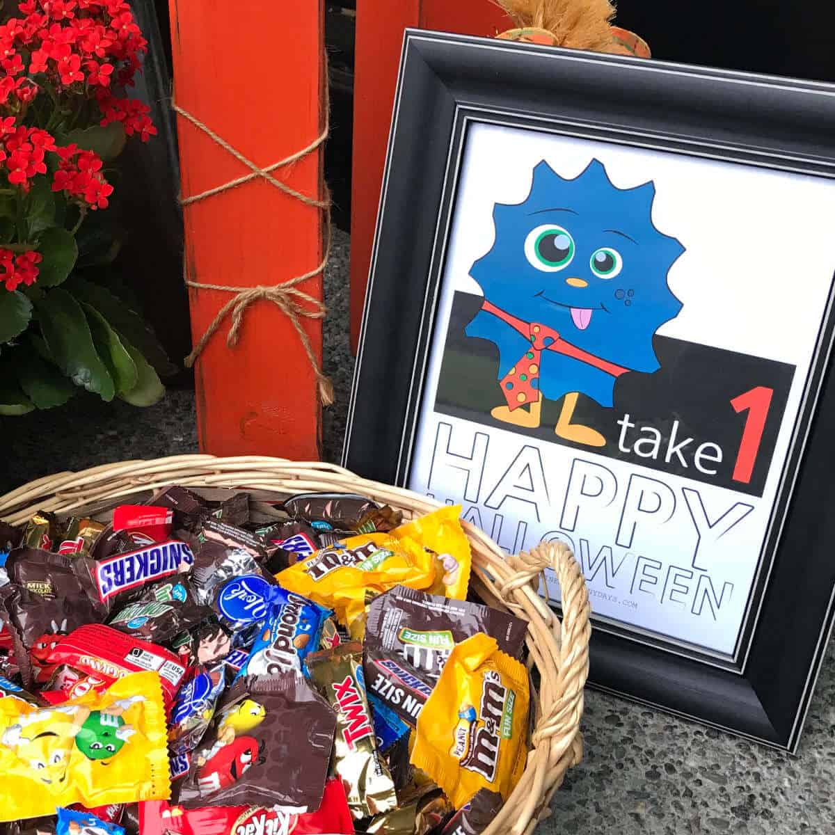 Framed printable sign that says Take 1, Happy Halloween next to a basket full of candy.