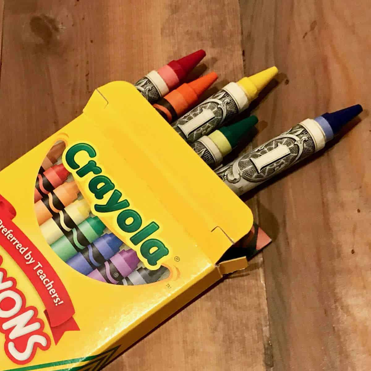 Money wrapped around crayons and the crayons coming out of a crayon box.