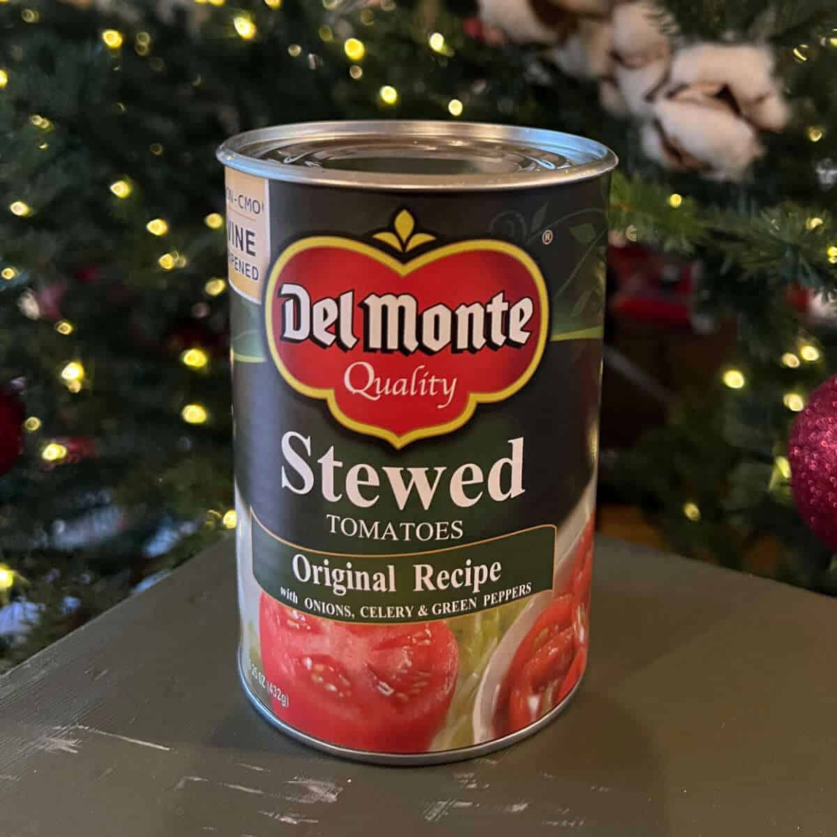 Can of stewed tomatoes sitting in front of a Christmas Tree.