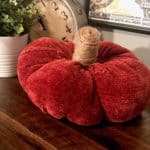 Pumpkin made out of a sweater and sitting on a dresser next to a plant and a clock.