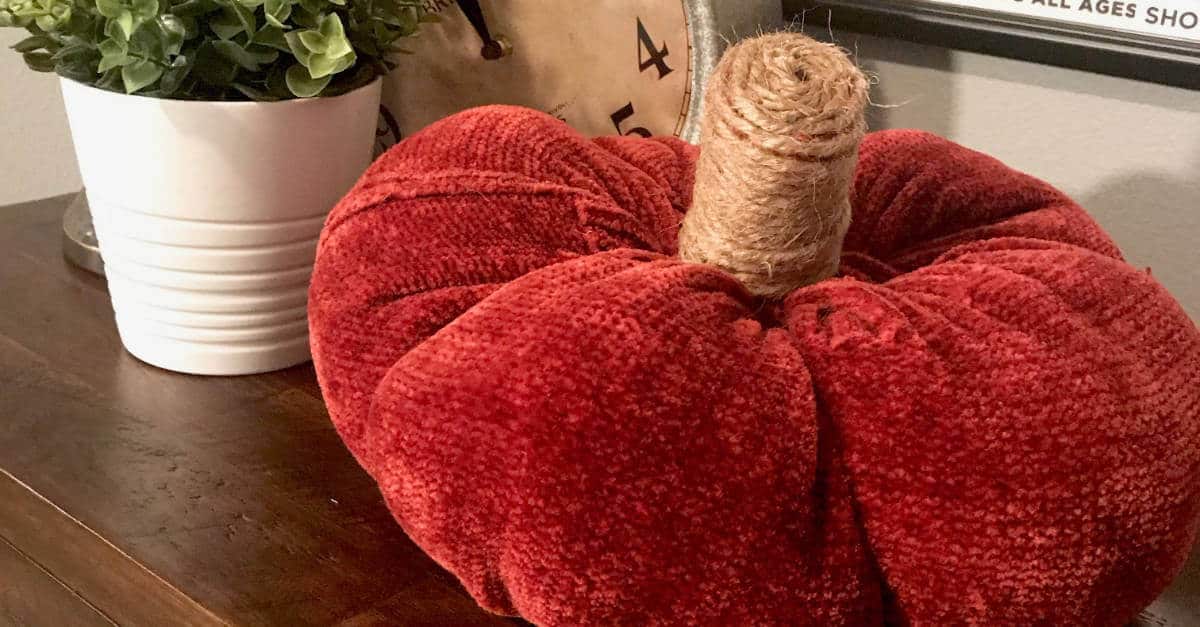 Large pumpkin made out of a sweater and placed on a dresser with a plant behind it.