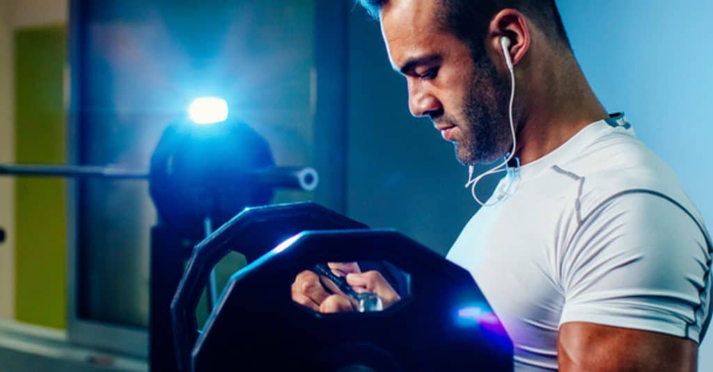 Man lifting weights with ear buds in.