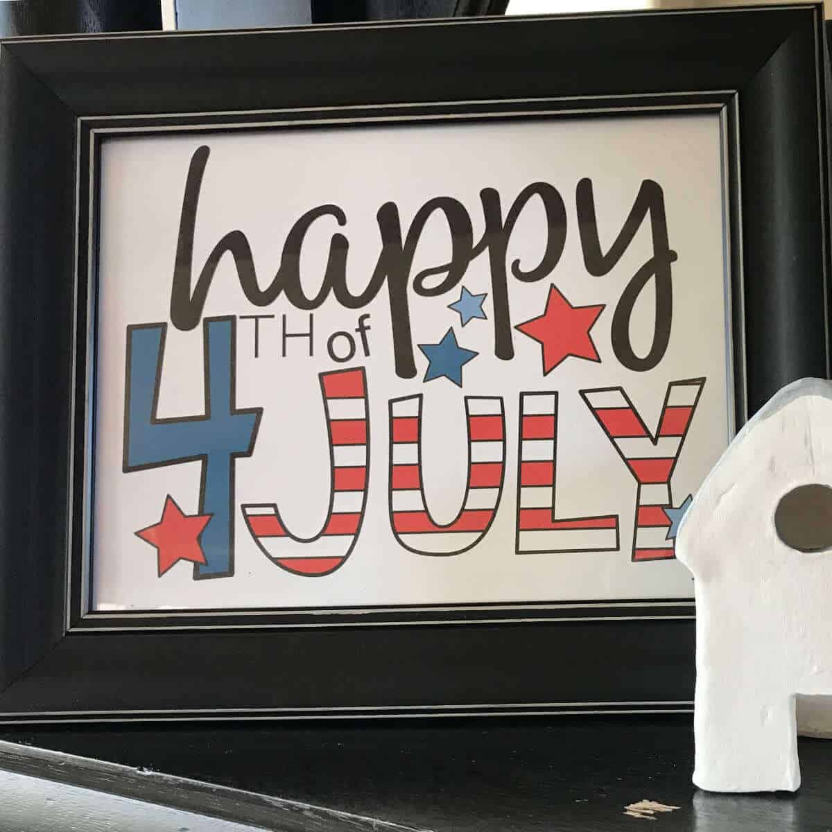 Printable Happy 4th of July Sign that is framed and on a fireplace mantel next to a ceramic house.