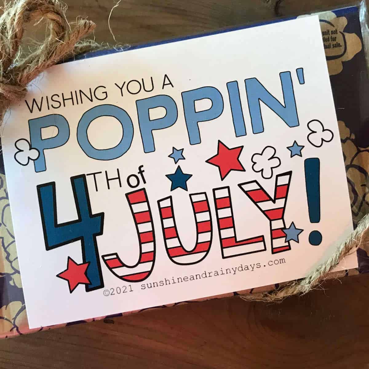 A bag of microwave popcorn with a fourth size piece of paper tied to it that says, Wishing You A Poppin' 4th of July!