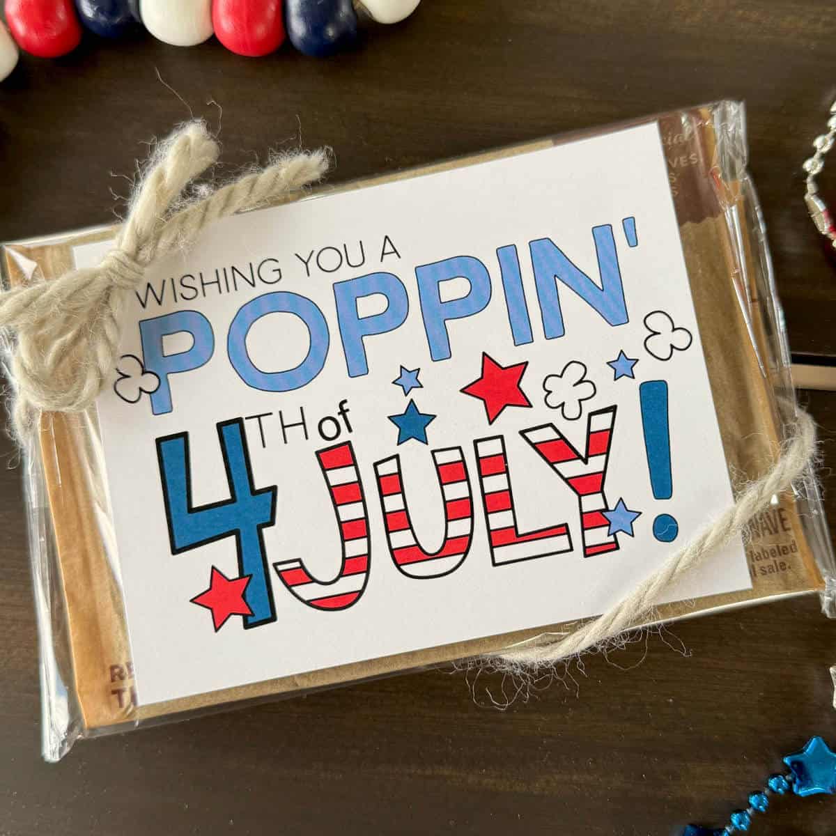 Image of an unpopped bag of microwave popcorn with a tag attached that says Wishing You A Poppin' 4th of July!