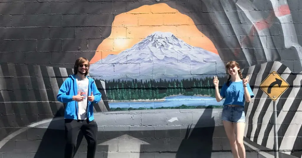 Teenagers taking photos in front of a mural painted on a building.