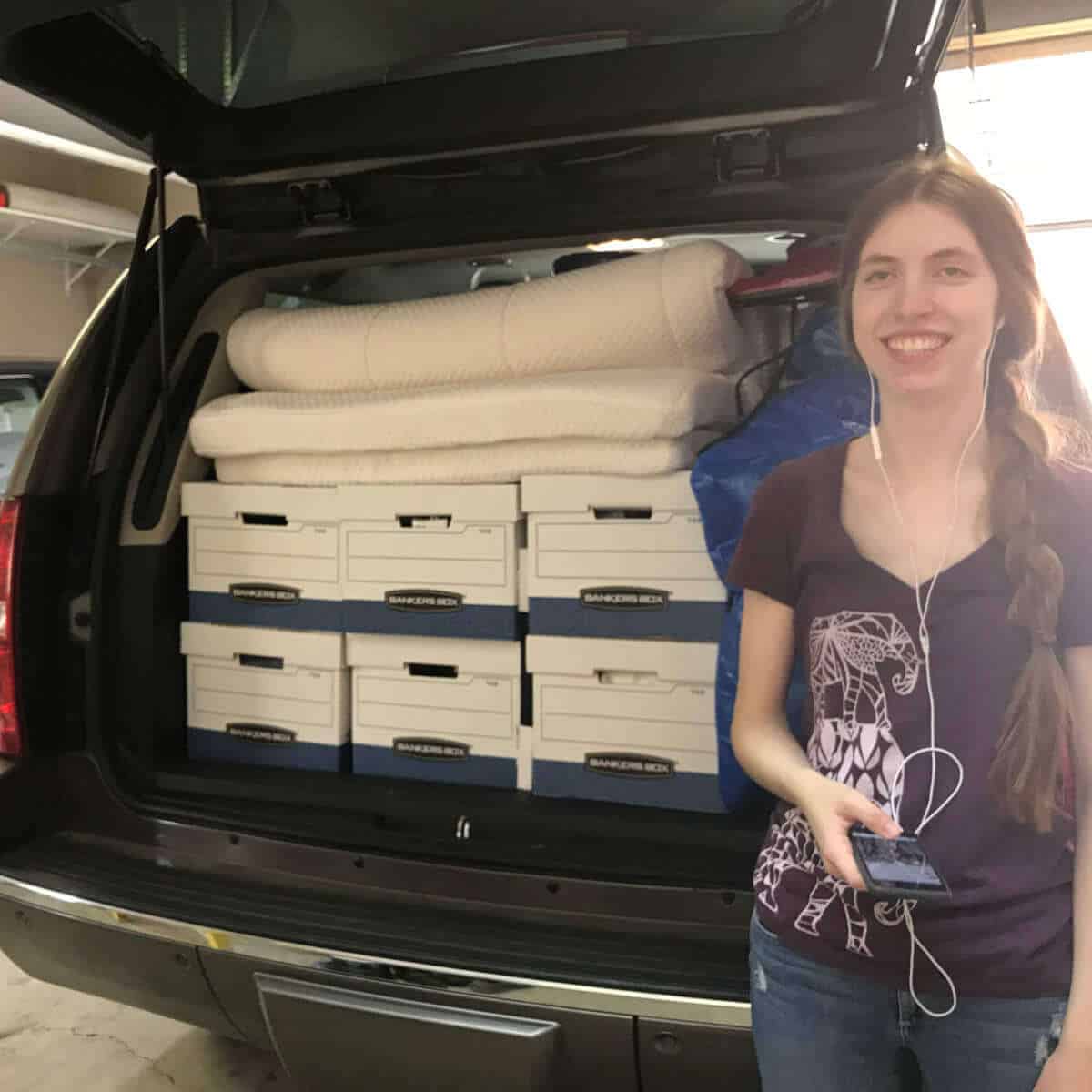 College girl standing in front of the back of a Tahoe filled with boxes for moving into a dorm room.