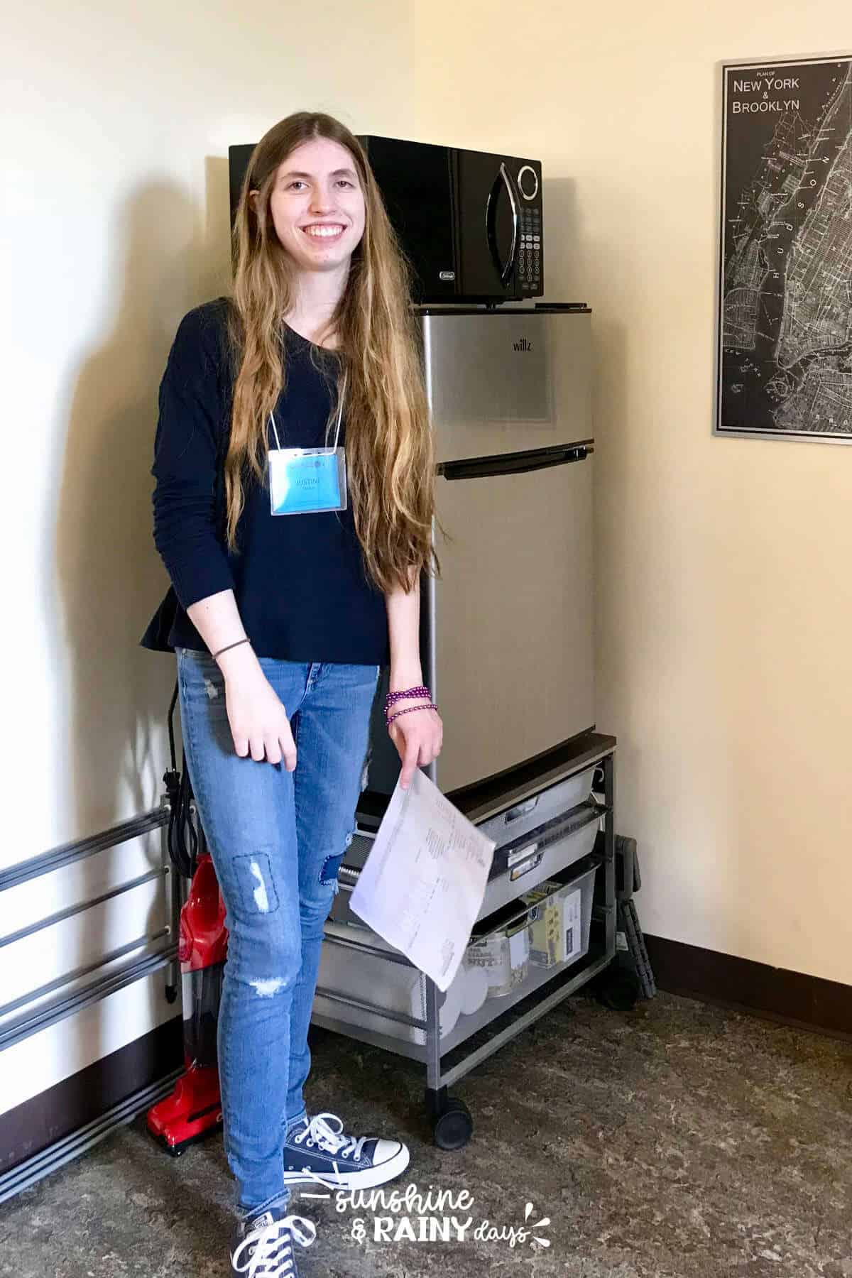 College girl standing in front of her refrigerator in a dorm room.