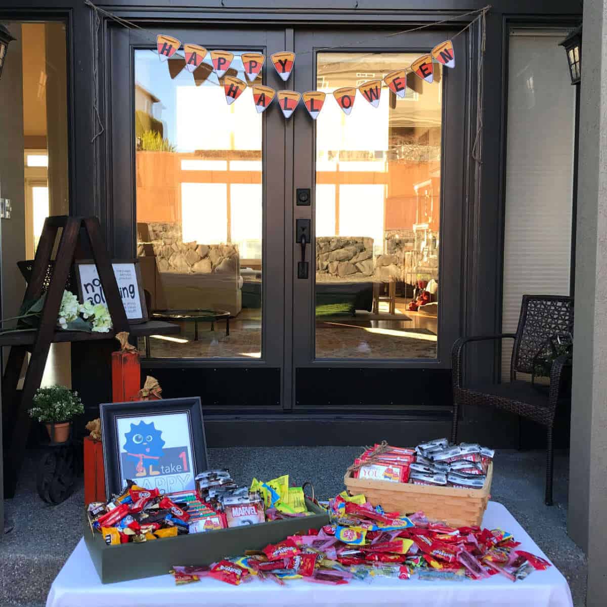 Trick-or-treat table full of treats at the front door with a Happy Halloween banner in the background.