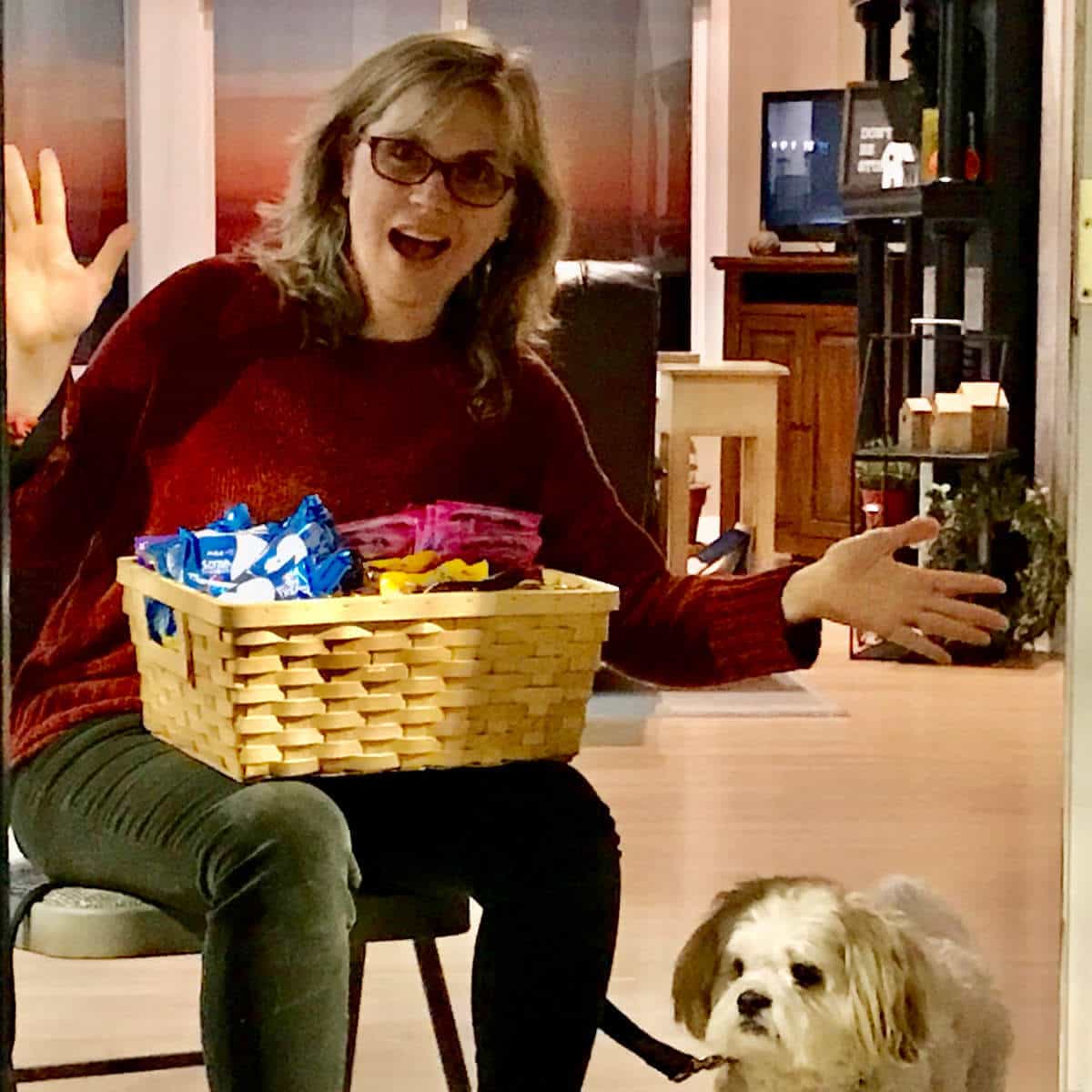 Lady sitting on a chair at her front door with a trick-or-treat basket and her dog.