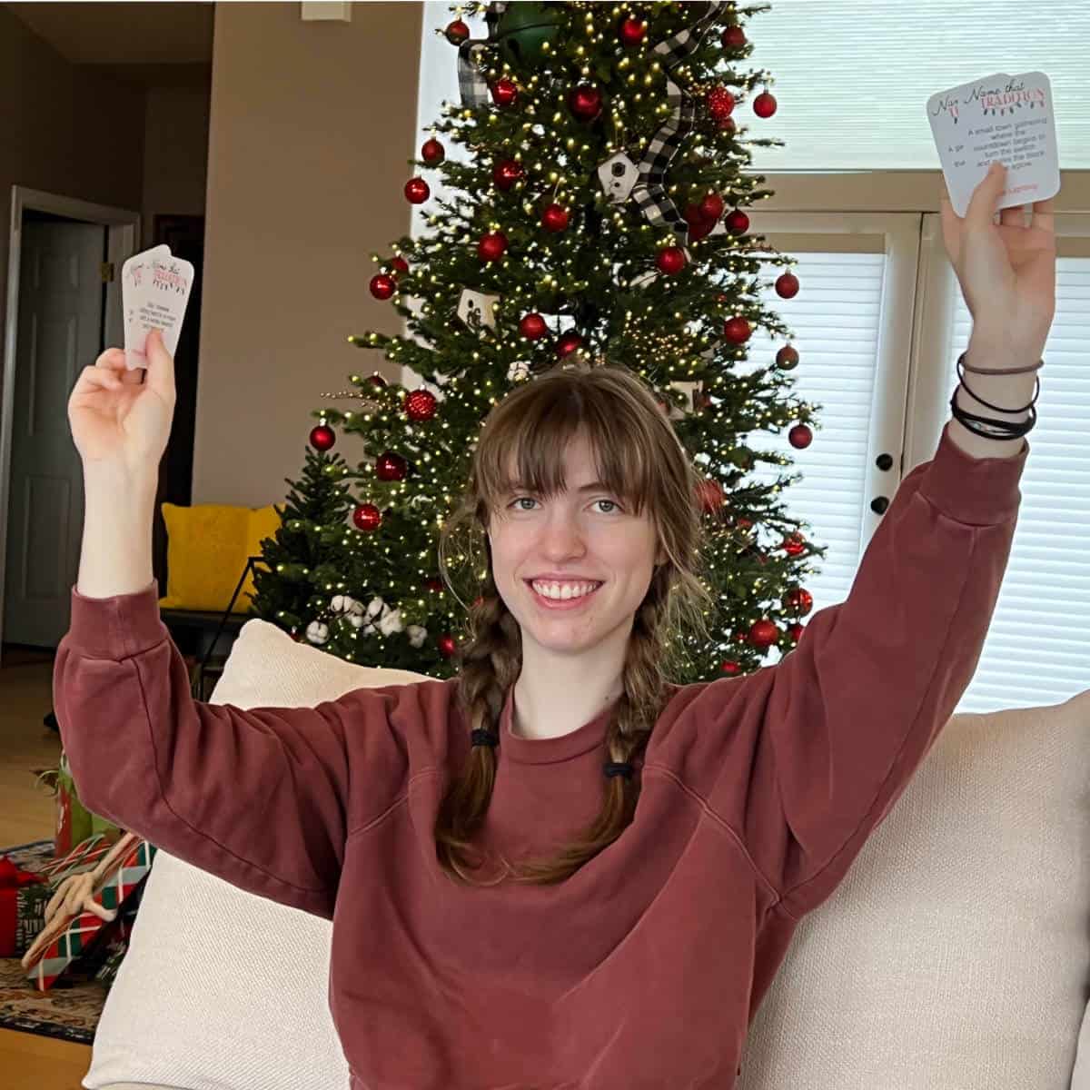 Girl holding up game cards in both hands while sitting on a couch with a Christmas tree in the background.
