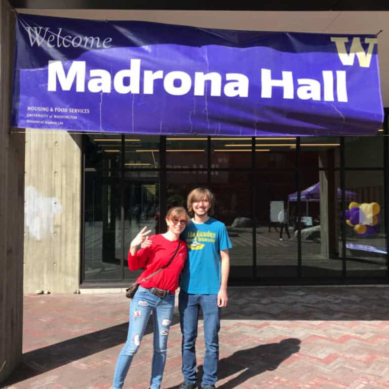 A college student and his mom in front of his new dorm hall.