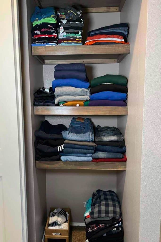 Clothes on shelves in a small closet.