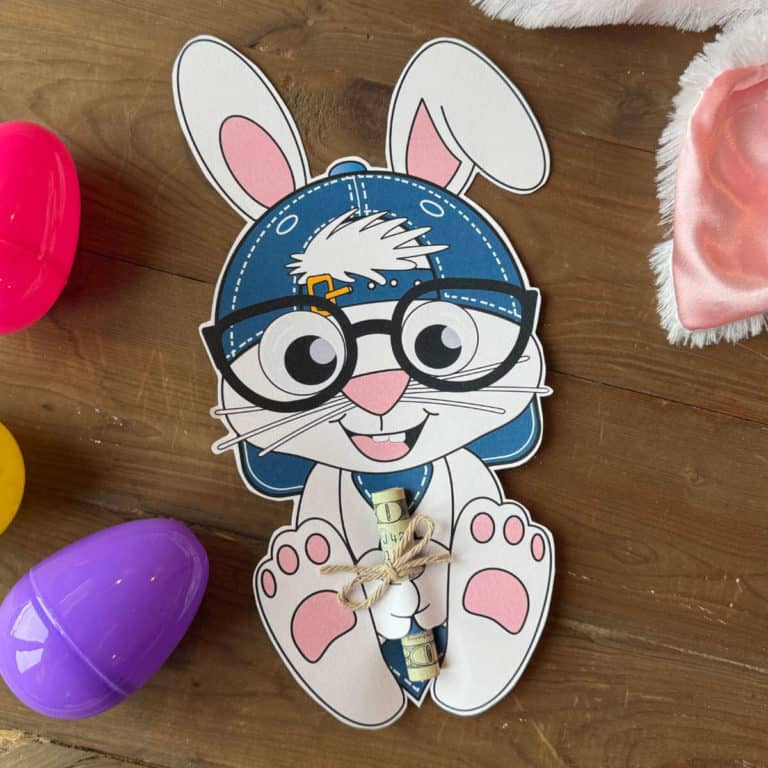 Printable Easter Bunny holding a rolled bill with plastic eggs and bunny ears nearby.