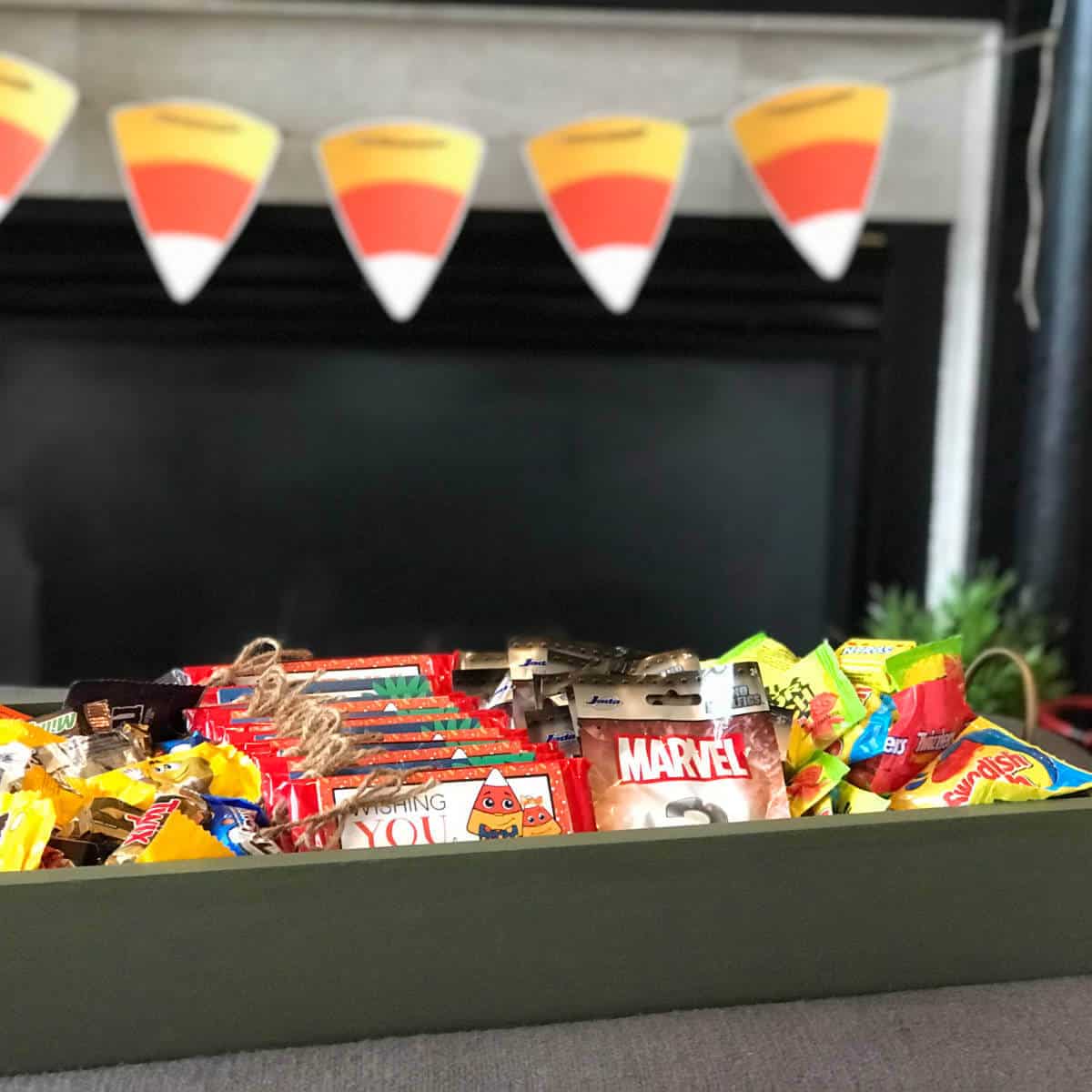 Wood tray full of trick-or-treat goodies with a candy corn banner in the background.