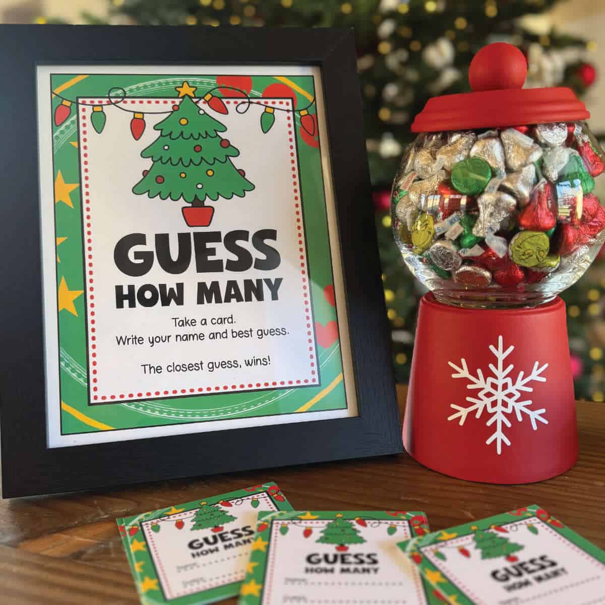 Guess How Many Christmas game sign next to guess cards and a candy dish full of candy Kisses.