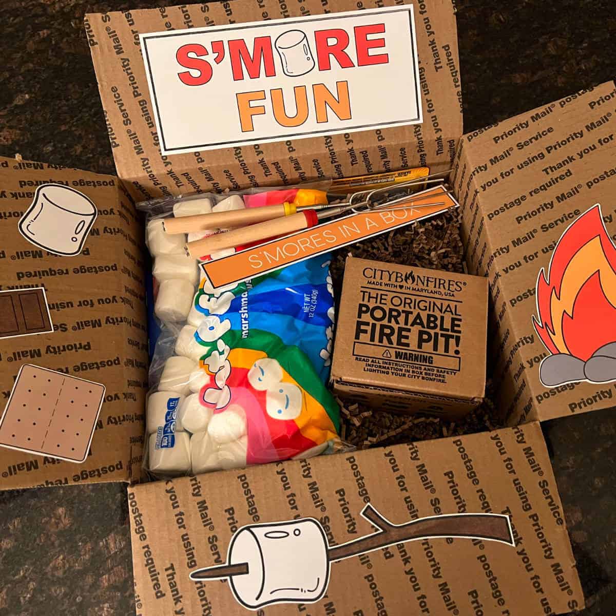 Picture of a box filled with ingredients to make s'mores with themed printable decor on the box flaps.