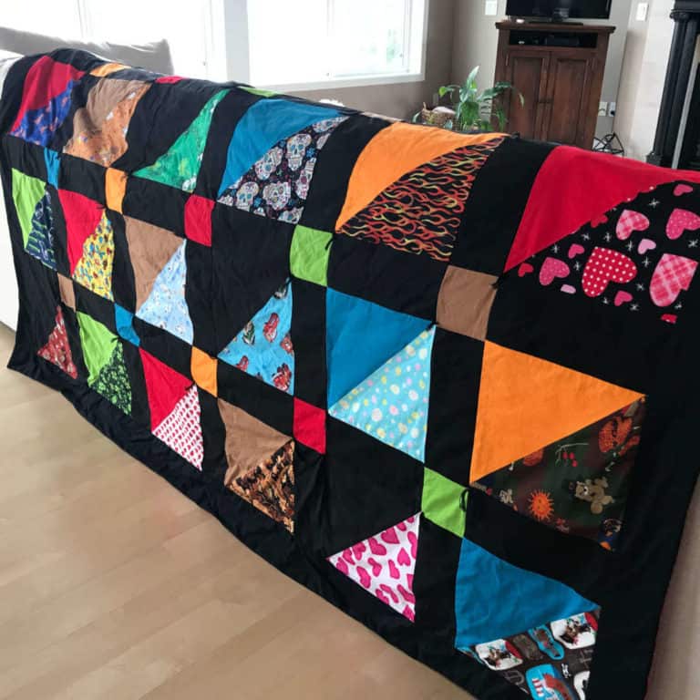 A quilt made out of dog bandanas, draped over the back of a couch.