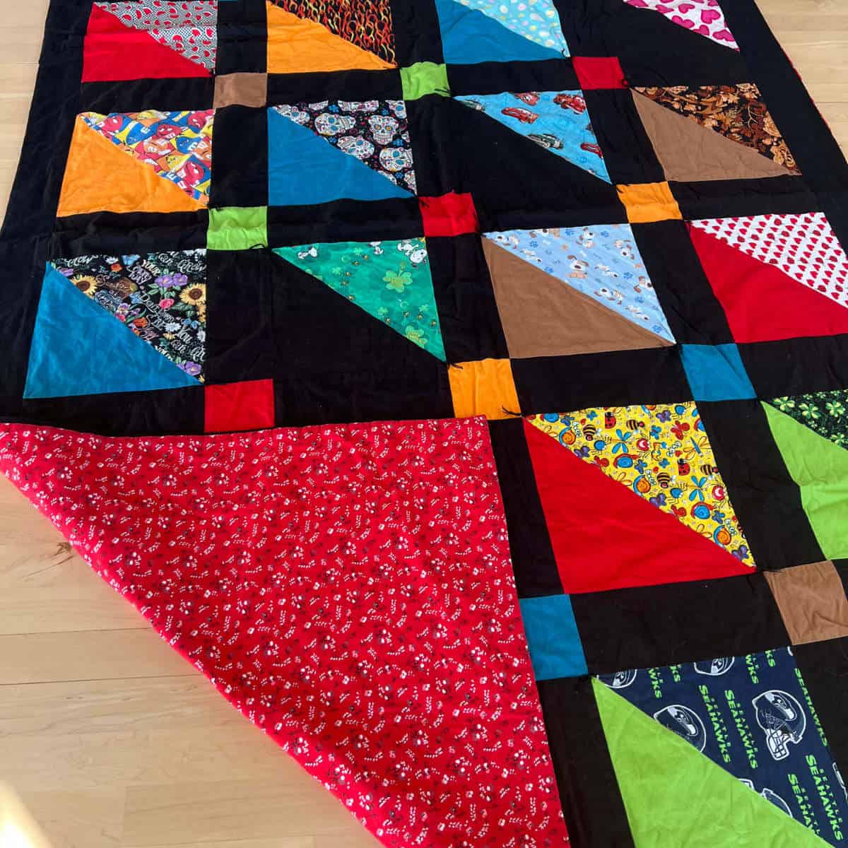 A quilt made out of dog bandanas with the corner folded up so you can see the back lining.