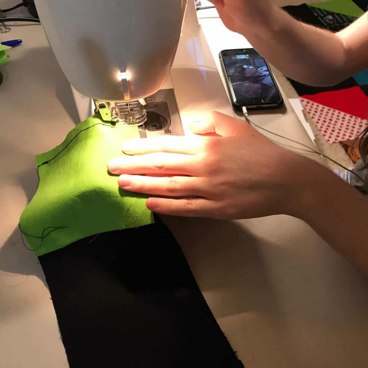 Girl's hands guiding pieces of a quilt on a sewing machine.