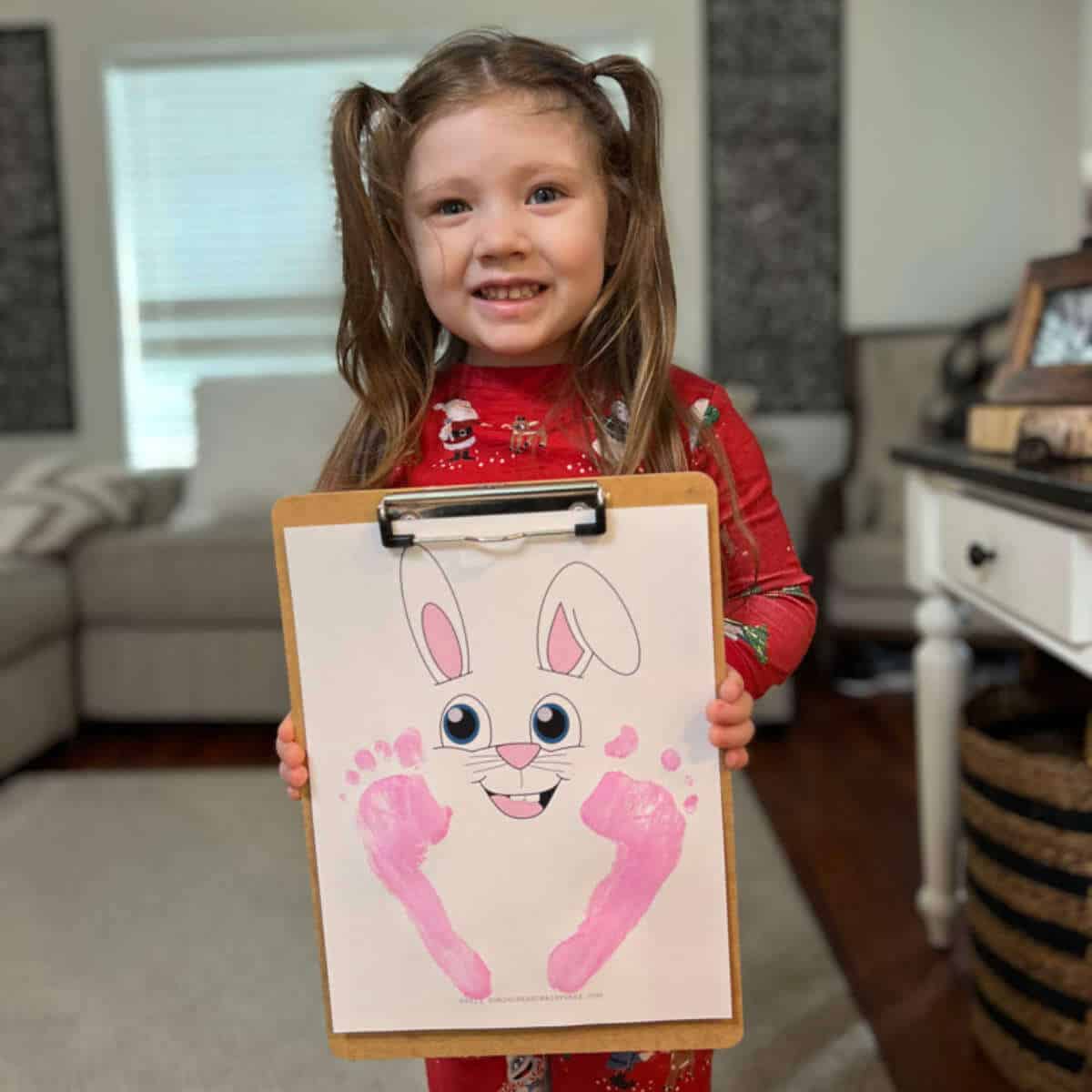 Little girl holding a clipboard with a printable page that has an Easter bunny face and the little girl's footprints on it.