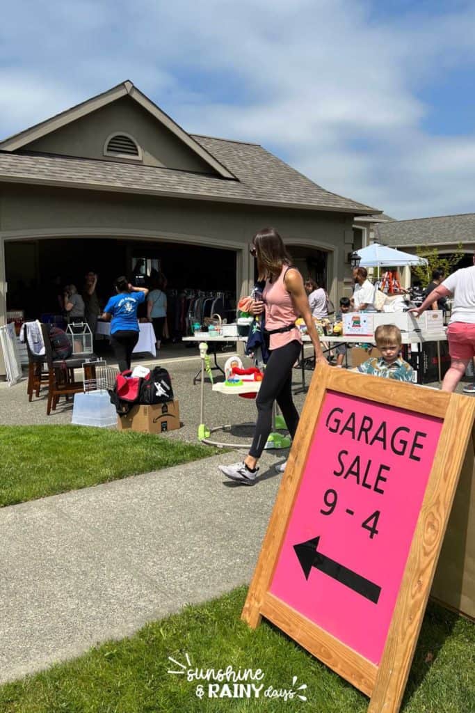 Garage sale sign in front of a busy garage sale.