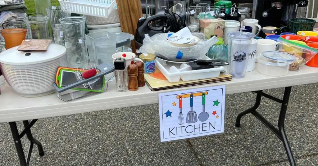 Kitchen sign on a table full of kitchen items at a garage sale.