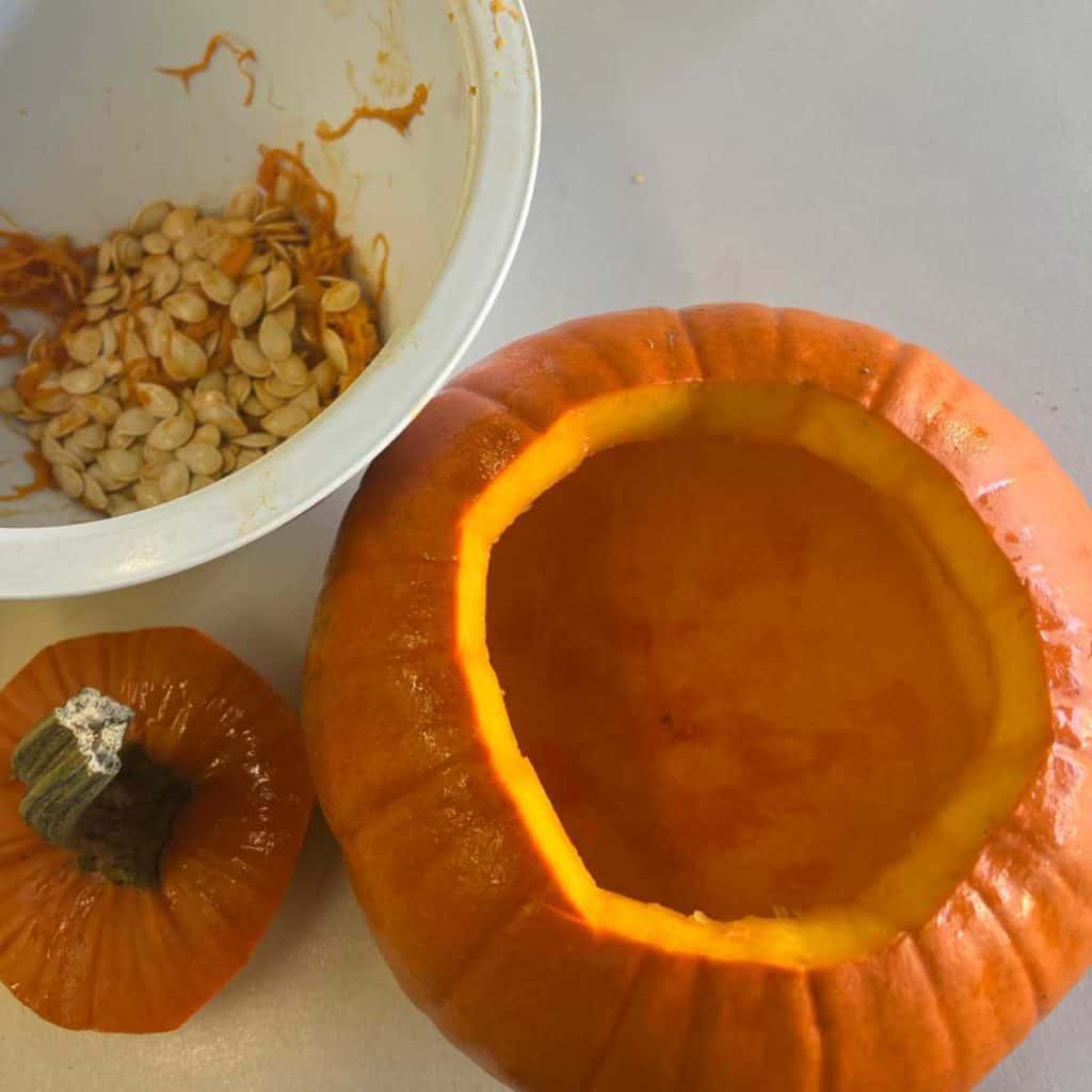 A pumpkin that has been cleaned out with a bowl of pumpkin seeds next to it.