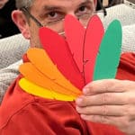 Man with glasses holding up colorful paper turkey feathers