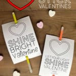 Printable tags with glow sticks attached sitting on a table with conversation hearts around them.