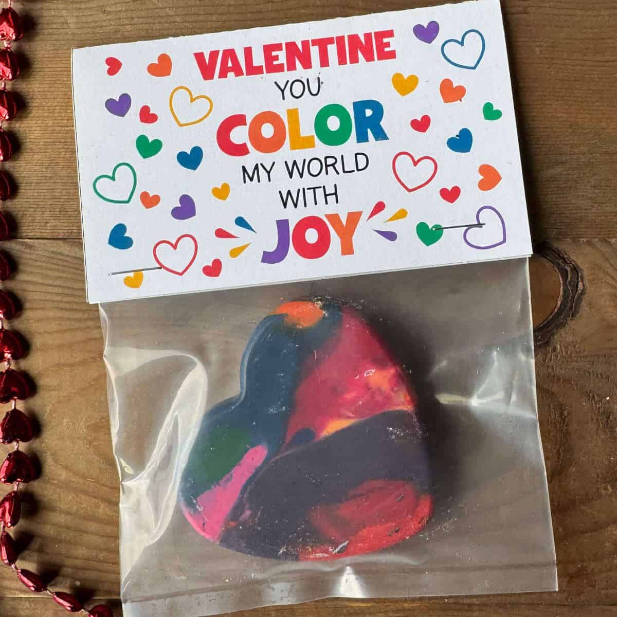 Heart made out of crayons, in a bag, with a bag topper that says Valentine you color my world with joy!