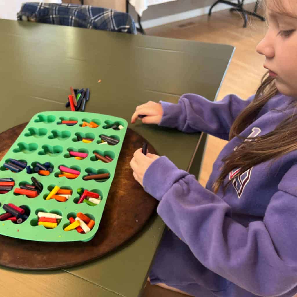 Little girl placing broken crayons into a mold for melting.