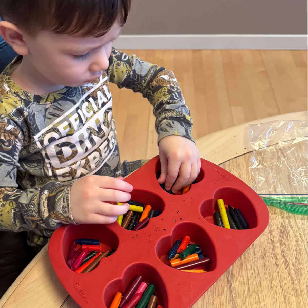 Little boy placing old crayons in a heart shaped silicone mold.